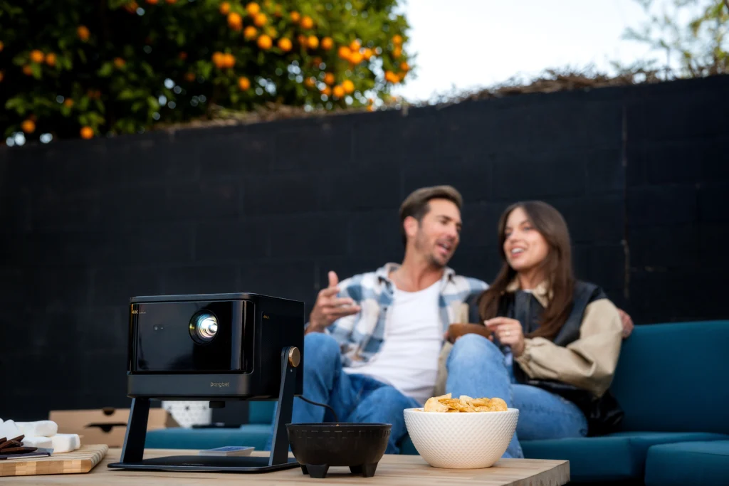 Dangbei DBOX02 projector on a table with snacks in front of a couple enjoying an outdoor movie night.