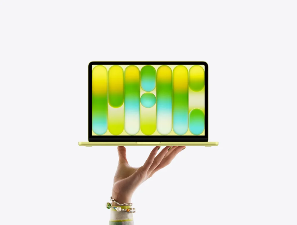 MacBook Neo in citrus color, balanced on fingertips of open hand, screen displaying colorful abstract pattern
